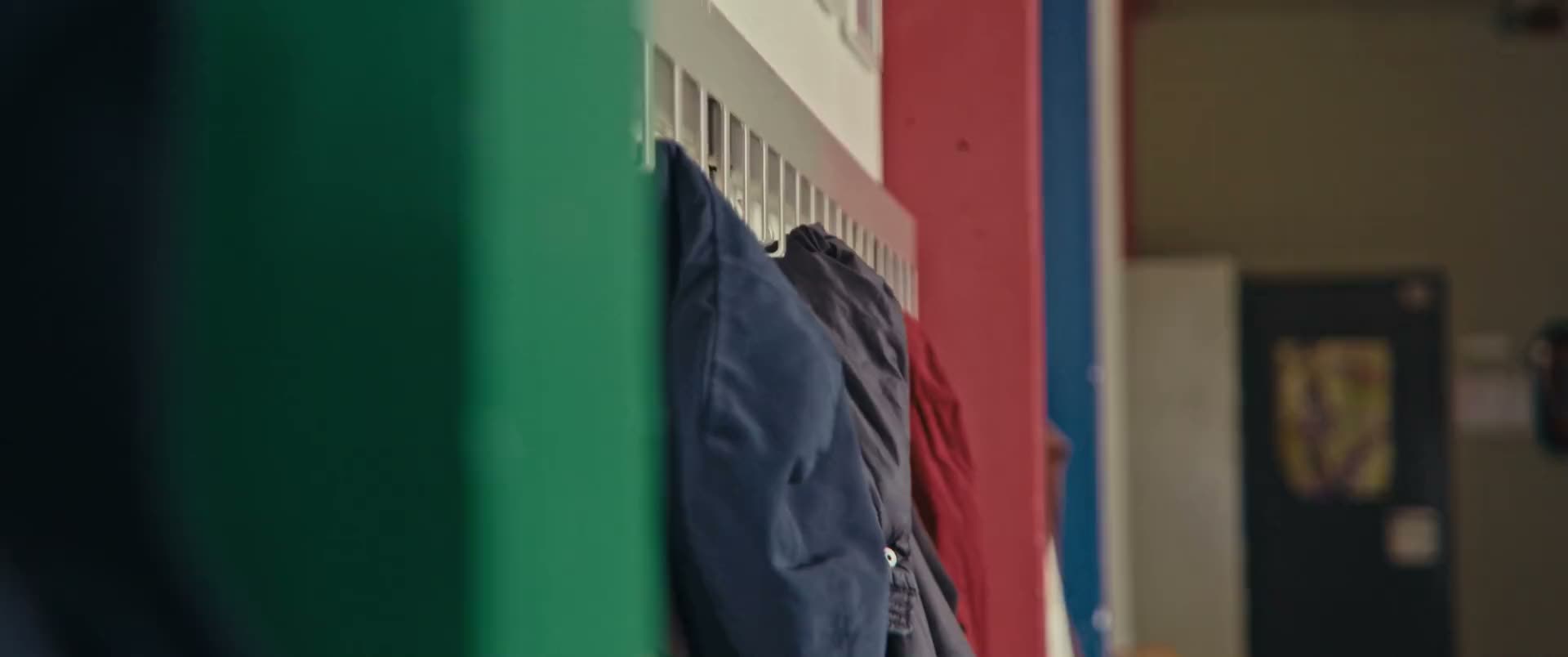 Een schoolgang met kapstokken en kleurrijke pijlers, een leerling loopt voorbij.